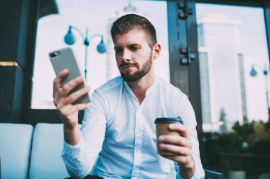 Beyaz gömlekli, işe yakın caddede oturan ve kahve molası sırasında cep telefonunu karıştıran düşük odaklı erkek yönetici açısı.