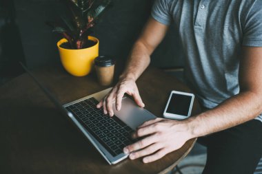 Uzaktan kumandalı kafeteryada çalışırken akıllı telefon saksısıyla masada otururken ve kahve içerken tanınmayan serbest çalışan erkek Netbook 'un üstünden.