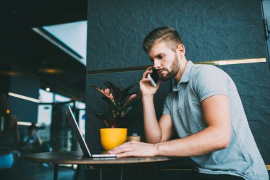 Düşünceli erkek serbest çalışanın iş sırasında açık kafede saksı ile masada otururken telefon görüşmesi ve internette sörf yapması.