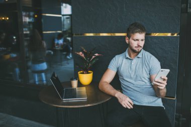 Kendine güveni tam erkek serbest çalışan cep telefonuna mesaj atıyor. Terasta çalışırken saksı çiçeği ve dizüstü bilgisayarla aynı masada oturuyor.