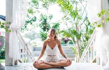 Gülümseyen genç kadın yoga yapıyor ve otelin dışında meditasyon yapıyor. Turizm, tatil ve hafta sonu kavramı. Güzel beyaz bir kız. Bali adasında huzurlu ve huzurlu bir yaşam tarzı. Güneşli bir gün