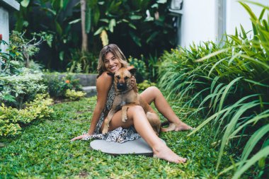 Otel bahçesinde sevimli köpeğe sarılan mutlu genç bir kadın. Turizm, tatil ve hafta sonu. Sahibi ve evcil hayvan ilişkisi ve dostluğu. Beyaz kız kameraya bakıyor. Idyllic ve sakin yaşam tarzı