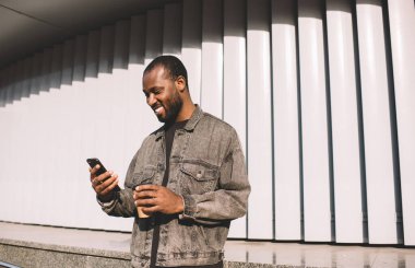 Gülümseyen seyahat blogcusu cep telefonuyla mesajlaşmanın keyfini çıkartıyor. Mobil ağ kurmak için boş zamanlarında, neşeli siyah hippi adam elinde kahve ile akıllı telefonuyla internet sitesine girip