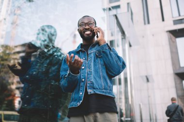 Şehir merkezindeki internet bağlantısını cep telefonu araması için kullanan neşeli siyah seyahat turisti, optik gözlüklü neşeli Afro-Amerikan hipster adam mobil uygulama üzerinden telefonla ararken gülümsüyor.