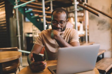 Bluetooth bağlantısı üzerinden medya dosyalarını paylaşmak için cep telefonu ve dizüstü bilgisayar kullanan yetenekli özgür metin yazarı, cep telefonundan SMS gönderirken e-posta alan Afrikalı Amerikalı erkek blogcu