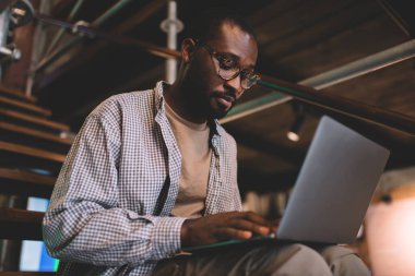 Klasik gözlüklü yetenekli Afro-Amerikalı adam modern dizüstü bilgisayarda WIFI kablosuz bağlantısını kablosuz kablosuz kablosuz kablosuz bağlantıyla geziyor, milenyum yazılım geliştiricisi bankacılık yapıyor.