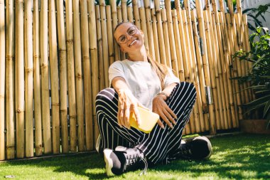 Mobil ağ kurmak için boş zamanlarında kameraya gülümseyen klasik gözlüklü neşeli kadın portresi, cep telefonlu mutlu Kafkasyalı hipster milenyumu