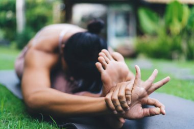 Yoga yapan bir kız, baş-diz öne kıvrılıp dışarıda poz veriyor. Sağlıklı yaşam tarzı kavramı. Spor giyimli genç bir kadın Bali adasındaki bulanık avluda spor minderinde yatıyor.
