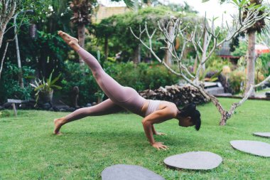 İnce Asyalı kızın açık havada yoga çalışmasının yan görüntüsü. Sağlıklı yaşam tarzı kavramı. Bali adasında spor giyimli ve çıplak ayaklı çekici esmer atletik kadın. Gündüz