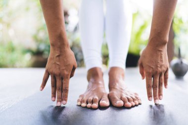 Yarı ayakta eğilme pozisyonunda yoga yapan bir kızın kısmi görüntüsü bulanık ahşap terasta. Sağlıklı bir yaşam tarzı. Spor giyinen ve spor minderinde çıplak ayaklı bir kadın. Bali adası. Güneşli bir gün