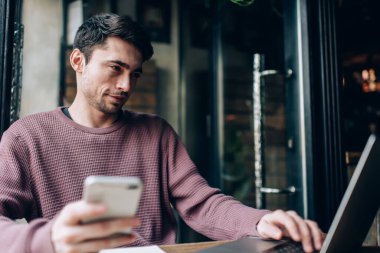 Modern dizüstü bilgisayar teknolojisi ve cep telefonu paylaşım medya dosyalarında birlikte çalışma alanındaki bluetooth bağlantısını kullanan beyaz yetenekli programcı, mobil ve netbook ağları olan genç hipster adam.