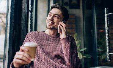 En iyi arkadaşı aramak ve onunla konuşmak için akıllı telefon uygulamasını kullanmak üzere paket kahve getiren neşeli erkek müşteri, kullan-at bardaklı neşeli hippi adam pozitif cep telefonu iletişiminin keyfini çıkarıyor.