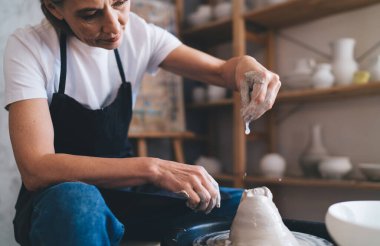 Sanat stüdyosundaki çömlek çarkının üzerinde kil kalıbı döşeyen Kafkas kadın üstadı odaklanmış. Küçük işletme ve girişimcilik kavramı. Ev hobisi, eğlence ve eğlence. İş önlüğü giyen kadın.