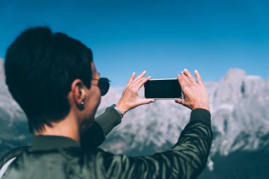 Genç bayan gezginin, akıllı telefon kamerasıyla doğa manzarasını fotoğraflamasının arka görüntüsü. Cep telefonuyla panoramik video çeken kadın.