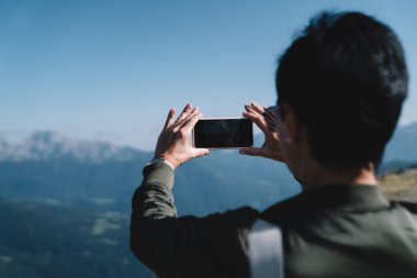Genç bayan gezginin, akıllı telefon kamerasıyla doğa manzarasını fotoğraflamasının arka görüntüsü. Cep telefonuyla panoramik video çeken kadın.