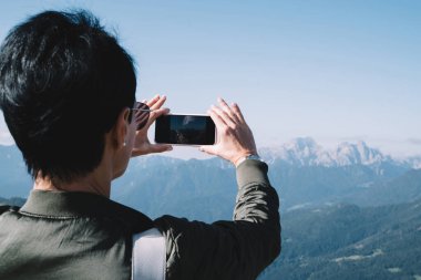 Genç bayan gezginin, akıllı telefon kamerasıyla doğa manzarasını fotoğraflamasının arka görüntüsü. Cep telefonuyla panoramik video çeken kadın.