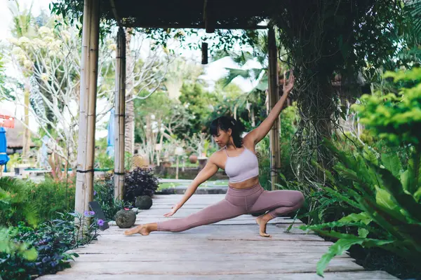 Stock image Asian girl practicing yoga in Triangle pose outdoor. Concept of harmony and mental health. Young beautiful focused athletic woman wearing sportswear on wooden terrace on Bali island