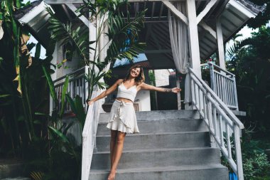Otelin merdivenlerinde durup dinlenen neşeli genç bir kadın. Turizm, tatil ve hafta sonu. Çekici beyaz kız kameraya bakıyor. Bali adasında huzurlu ve huzurlu bir yaşam tarzı. Güneşli bir gün