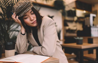 Milenyum Asyalı güzel bir kız kafede kitap okuyor ya da bir şeye bakıyor. Masada oturan genç, düşünceli esmer kadın. Dinlenmek, boş zaman ve boş zaman kavramı. Modern kadın yaşam tarzı