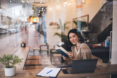 Asyalı kız defterin sayfasını çeviriyor ve kafede kameraya bakıyor. Genç milenyum esmer kadın kulaklık takıyor masada açık dizüstü bilgisayarla oturuyor. Serbest ve uzaktan kumandalı. Modern kadın yaşam tarzı