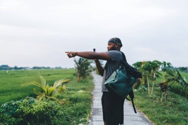 Turistik sırt çantalı Afrikalı Amerikalı seyahat blogcusu vlog içeriği çekmek için profesyonel teknoloji kullanıyor ve Endonezya 'daki pirinç tarlalarını işaret eden hipster çocuk Bali' de yaz tatilleri hakkında konuşuyor.