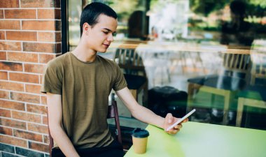 Kahve molası sırasında kafedeki masada oturan ve cep telefonunda internet gezen genç adam.