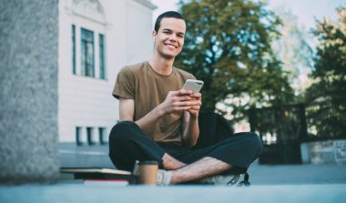 Gülümseyen erkek kameraya bakıyor ve Lotus 'ta oturuyor. Sosyal ağlardaki bildirimleri kontrol etmek için cep telefonu kullanıyor.