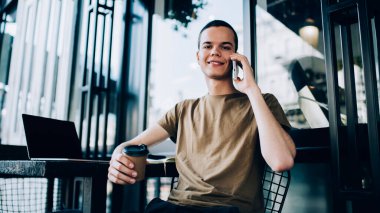 Cafe 'nin terasında netbook' la oturmuş kameraya bakarken cep telefonuyla konuşan ve kahve içen neşeli serbest çalışan adamdan.