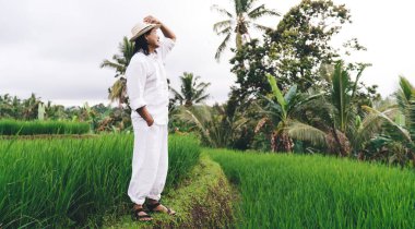 Şapkalı sıradan bir adam Bali 'de hasat mevsiminde çeltik ekimini ziyaret ederken, yetişkin bir erkek çiftçi pirinç tarlalarıyla tarım işine baktığı için Endonezya' ya uluslararası bir gezi düzenliyor.