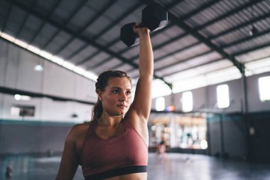 Sportif giyinen kararlı beyaz kadın spor salonunda el kasları üzerinde çalışırken halter kullanıyor, ağırlığını kaldıran güçlü profesyonel kadın - vücudunu tonusta tutmak için üst kol pazılarını eğitiyor.