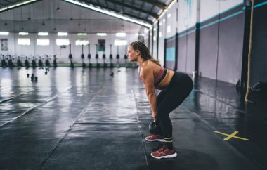 Spor eşofmanlı beyaz tenli güçlü bir sporcunun yan görünüşü ağırlık kaldırma antrenmanını spor salonunda yapıyor. Dayanıklılıkla egzersiz yapan zayıf bir kadın.