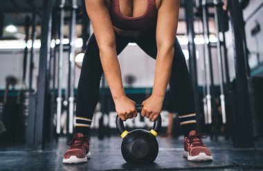 Spor stüdyosunda kettlebell halter tutan kadın sporcu. Spor antrenmanında dayanıklılık ve çaba. Halter egzersizi yapan ve tonusta kas tutmak için antrenman yapan tanınmamış bir kadın.