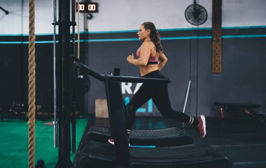 Spor salonundaki simülatör ekipmanlarında koşan sportif bir kadın. Dayanıklılık ve çaba, sağlıklı yaşam tarzına ulaşan zayıf formda bir kız. Koşu bandında mükemmel vücut ve vücut yapısını korumak için koşuyor.