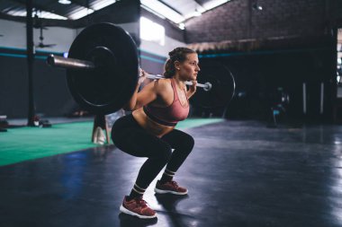 Spor stüdyosunda halter egzersizi yaparken vücut gücünü kontrol eden güçlü bir bayan sporcu spor yaparken halter malzemesi kullanan aktif bir kadın sağlıklı yaşam tarzını korumak için beden eğitimi sırasında halter ekipmanı kullanıyor.