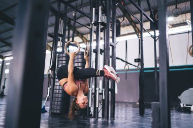 Profesyonel jimnastik yüzükleriyle gülümseyen heyecanlı bayan sporcu. Sportif ve sağlıklı yaşam tarzından memnun. Spor salonunda eşofmanlı vücut geliştirici.
