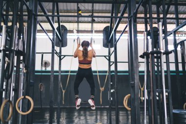 Genç, kaslı bir kadın jimnastik yüzükleri üzerinde yoğun idman yapıyor - fitness ve spor konsepti, eşofmanlı vücut geliştiriciler için arka görüş - spor ekipmanlarıyla barfiks çekiyor - dayanıklılık