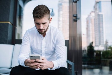 Resmi olarak ciddi genç girişimci rahat koltukta oturup, kafede proje üzerinde çalışırken akıllı telefonla mesajlaşır.