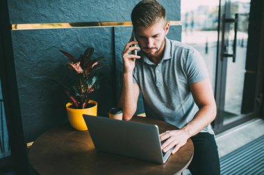 İnternetteki kafe çalışmaları sırasında çiçek saksısı ile masada otururken konsantre bir erkek telefonda konuşuyor ve netbook 'ta daktilo ediyor.