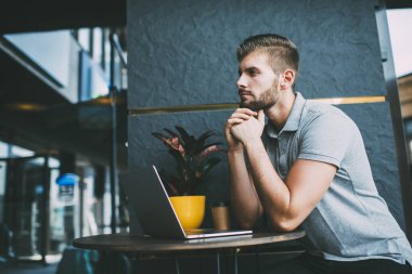 Çevrimiçi kafe çalışmaları sırasında netbook ile masada otururken ellerini kavuşturup mesafeye bakan düşünceli bir erkeğin yan görüntüsü