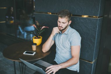 Sokak kafeteryasında yuvarlak masada oturup dizüstü bilgisayarla uzaktan kumandayla iş yapan konsantre bir erkek çenesi.
