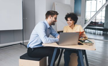 İş kadını defterde bir şey gösteriyor ve erkek arkadaşına bakıyor. İş birliği ve takım çalışması. Genç, gülümseyen Kafkas milenyum insanları büroda masa başında. Modern başarılı insanlar