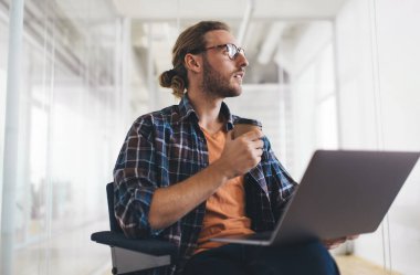 Uzaktan kumandalı iş sırasında internet programlama hakkında düşünen düşünceli bir adam. Laptop bilgisayarı ve kahveyle birlikte bin yıllık blog yazarı. Düşünceli bir görünüm sergilemek için.