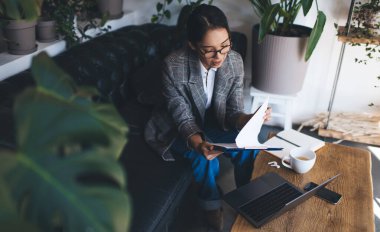 Yazılı raporu analiz ederken dijital netbook teknolojisini kullanmak için internet bağlantısıyla birlikte çalışma alanında iş planı oluşturan klasik görüş koruması altında zeki bir kadın.