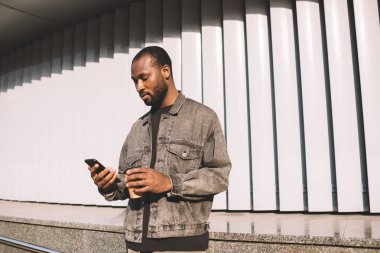 Millennial hipster 'lı adam internet üzerinden rezervasyon ve bankacılık yapmak için akıllı telefondan Afrikalı Amerikalı adam sosyal ağlarda internet iletişimi için mobil cihaz kullanıyor.