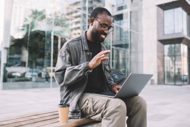 Mutlu koyu tenli adam, dijital göçebe hakkında konuşan neşeli bilişim teknolojisi profesyonel video bloğu ile modern dizüstü bilgisayarda uzaktan çalışırken olumlu bir video çağrısı alıyor.