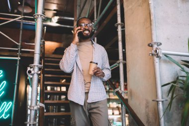 Optik gözlüklü neşeli siyahi hippi arkadaş cep telefonuyla gülümsüyor. Boş zamanlarında sohbet ediyor. Afro-amerikalı mutlu bir adam.