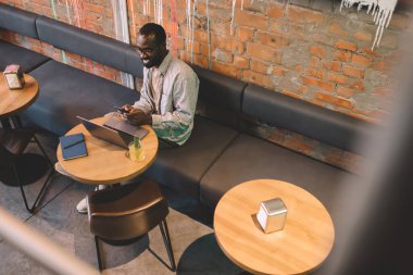 Bluetooth bağlantısı üzerinden medya dosyalarını paylaşmak için cep telefonu ve dizüstü bilgisayar kullanan neşeli serbest yazar, cep telefonuyla SMS gönderirken gelen e-postaları kontrol eden mutlu erkek blogcuların üst görünümü