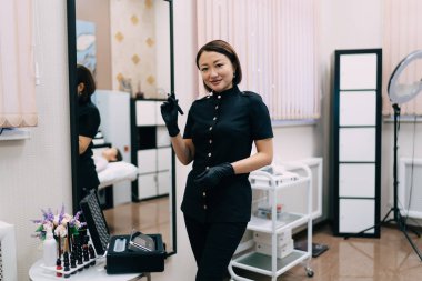 Kaş makyajı için iğne aleti olan bir kadın güzellik uzmanı ya da kameraya bakan bir mikropçu. Eldiven takan gülümseyen Asyalı kadın üstat. Güzellik konsepti. Modern güzellik salonunun içi.