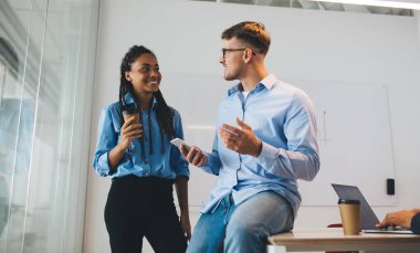 Kendine güvenen erkek ve bayan meslektaşlar şık günlük kıyafetler içinde iş yerinde akıllı telefon hareketliliğini tartışıyorlar şirket arkadaşlığının tadını çıkarıyorlar, mutlu ortaklar cep telefonuyla ofis ağı kurmaktan bahsediyorlar.
