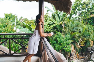 Hafta sonu dinlenmek için havluyla gezen çekici Koreli kadın, kahve fincanı ile kaygısız kadın güzellik prosedürleri hakkında hayal kuran sağlıklı yaşam ve cilt tazeleyici.